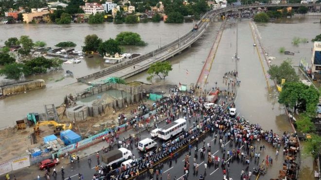 Индийские прохожие и путешественники собираются 2 декабря 2015 года, когда в конце шоссе в Ченнаи проходит круг наводнений.