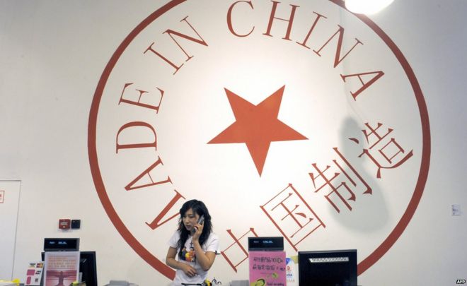 Женщина разговаривает по телефону у прилавка магазина в Пекине 18 июня 2009 года с огромным логотипом с надписью «Сделано в Китае» на стене