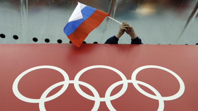 Torcedor com bandeira russa diante de logo olímpico
