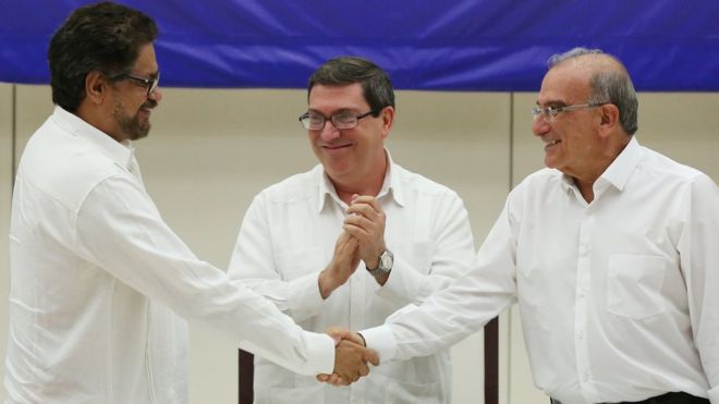 El principal negociador de las FARC, Iván Márquez (izq.) se da la mano con el principal negociador del gobierno de Colombia, Humberto de la Calle, ante la mirada sonriente del ministro de Relaciones Exteriores de Cuba, Bruno Rodríguez, tras firmar el documento final de la paz, en La Habana.