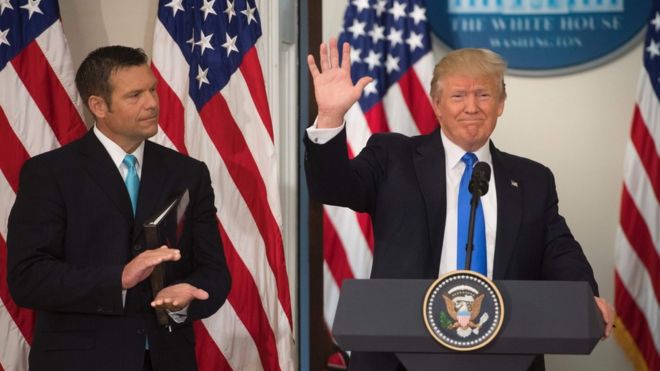 Президент США Дональд Трамп машет рукой после выступления вместе с госсекретарем штата Канзас Крисом Кобачем (слева) во время первого заседания Президентской консультативной комиссии по вопросам честности выборов в административном здании Эйзенхауэра