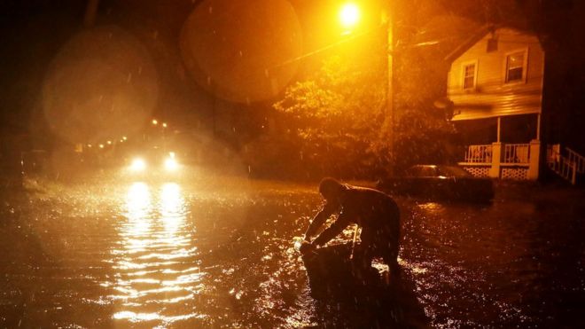 A man holds a small tin boat in rising flood waters