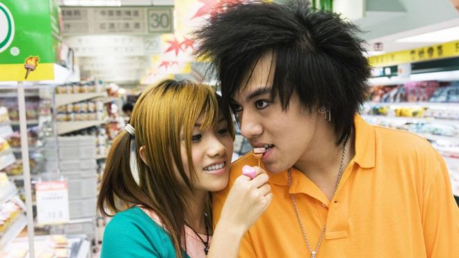Casal de jovens japoneses; moça dá uma comida na boca do namorado