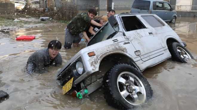 Residents try to upright a vehicle stuck in a flood hit area in Kurashiki