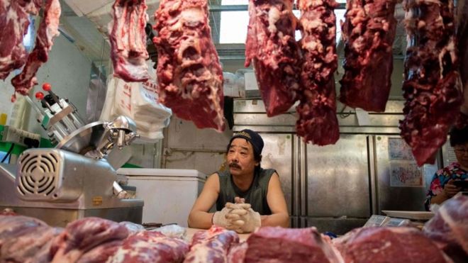 Мясник смотрит на мясо, висящее в магазине в Китае