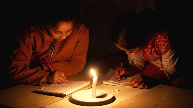 Девочки из числа палестинских беженцев учатся при свечах в временном доме их семьи во время отключения электричества в лагере беженцев Хан-Юнис в южной части сектора Газа (23 апреля 2017 года)