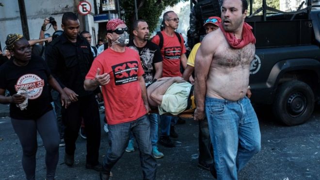 Спасатели несут человека, пострадавшего во время столкновений после акции протеста против жестких мер у здания Ассамблеи штата Рио-де-Жанейро