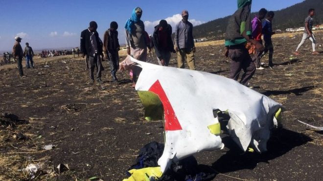 People walk past a part of the wreckage at the scene of the Ethiopian Airlines Flight ET302 plane crash