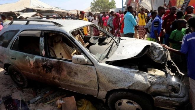 Civilians stand near a car destroyed in an explosion at the Madina district of Somalia (19 February 2017)