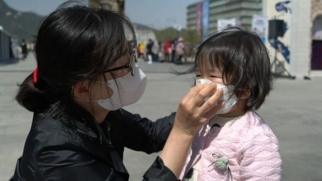Женщина помогает ребенку надеть маску в Сеуле