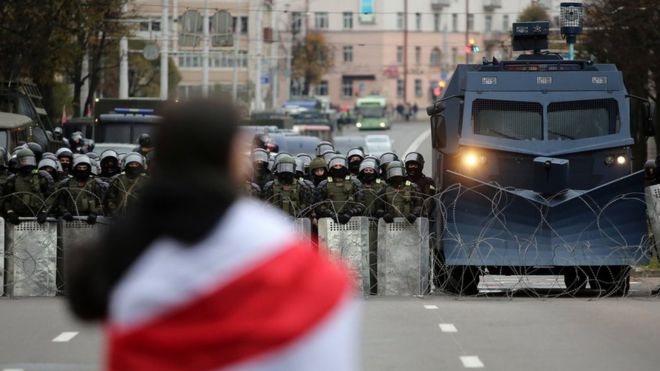 A protester with a flag stands in front of Belarusian policemen and a water cannon that block a road during a rally against government and President Lukashenko in Minsk, Belarus, 25 October 2020