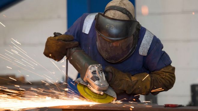 Sparks are seen as a man uses an angle grinder to cut and polish steel in a factory