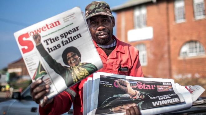 Продавец газет позирует с газетами на следующий день после смерти южноафриканского борца против апартеида Винни Мадикизела-Манделы в Йоханнесбурге 3 апреля 2018 года