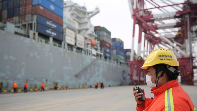 A masked foreman gives orders to other workers serving a container ship upon its arrival in a port in Qingdao in east China's Shandong province Tuesday, Feb. 04, 2020.-