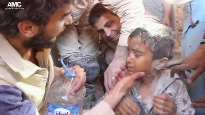 Young boy being given water after being rescued from rubble
