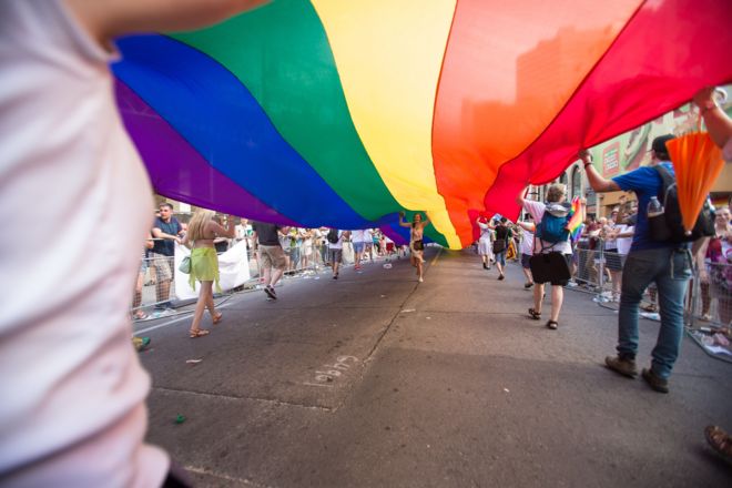 Женщина бежит под гигантским радужным флагом во время парада WorldPride 2014 в Торонто, Канада,