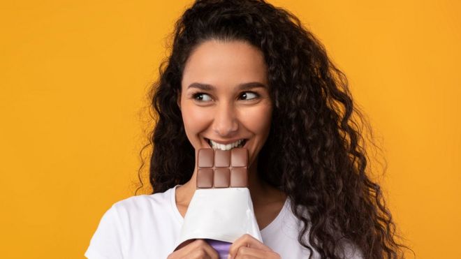 Una mujer sonriente muerde una barra de chocolate