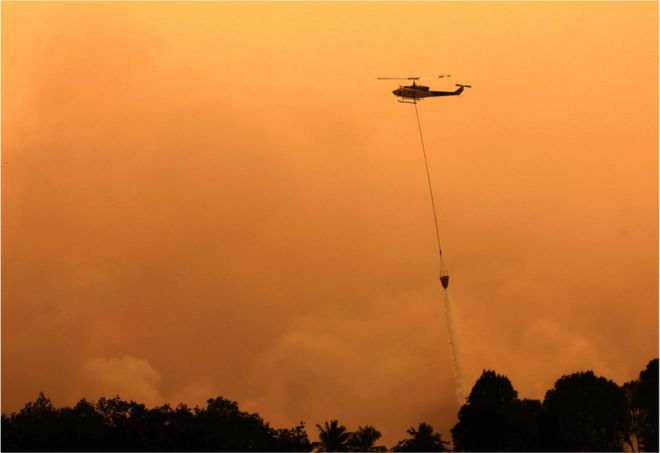 Вертолет сбрасывает воду, чтобы погасить бушующий пожар в Оган Комеринг Илир, провинция Южная Суматра, Индонезия, 13 сентября 2015 года