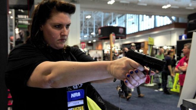 Una mujer prueba un arma en una exposición.