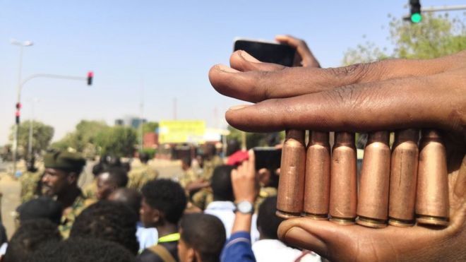 Суданский протестующий показывает патроны от пуль, когда другие собираются перед силами безопасности во время демонстрации в районе военного штаба в столице Хартум 8 апреля 2019 года