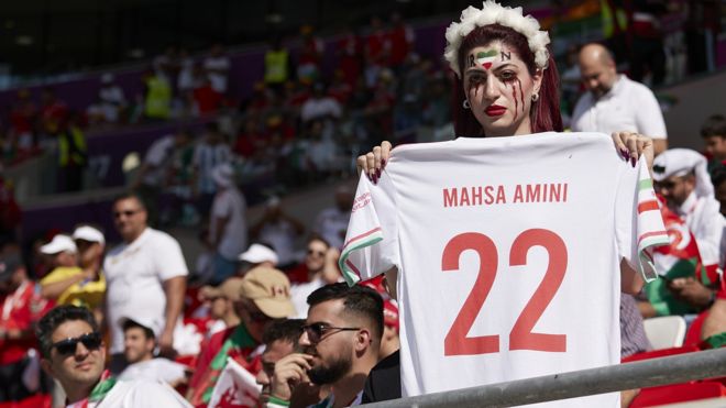 An Iranian football fan holds a football shirt with the name 'Mahsa Amini' on it