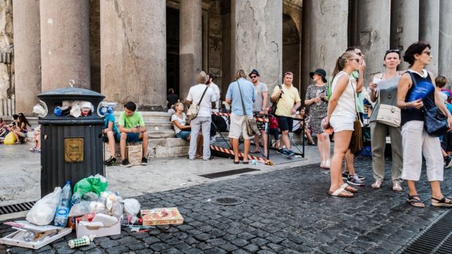 Туристы стоят возле мусорной корзины, переполненной отходами, перед Древним Пантеоном, в центре Рима 27 июля 2015 года