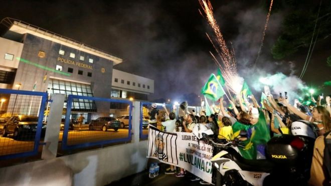 Демонстранты против Лулы празднуют, как бывший президент Бразилии Луис Инасиу Лула да Силва прибывает в штаб-квартиру Федеральной полиции в Куритибе, Бразилия