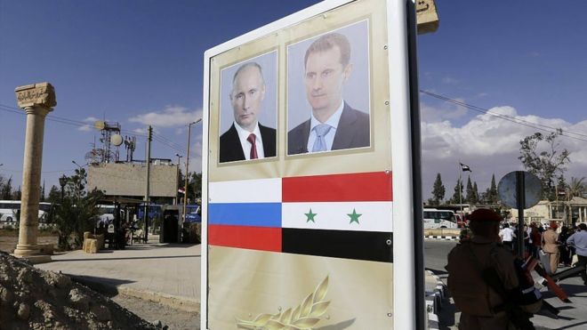 Плакат с портретом президента Сирии Башара Асада (R) и президента России Владимира Путина перед музыкальным концертом в древнем театре разрушенной в Сирии Пальмиры 6 мая 2016 года.
