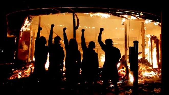 Manifestantes son vistos fuera de una licorería en llamas
