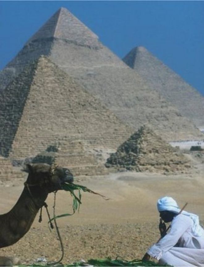 Перед пирамидами сидит мужчина с верблюдом
