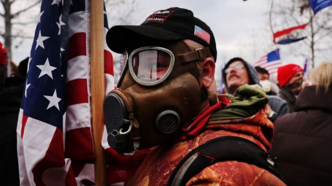Trump supporter seen in a gas mask holding a US flag