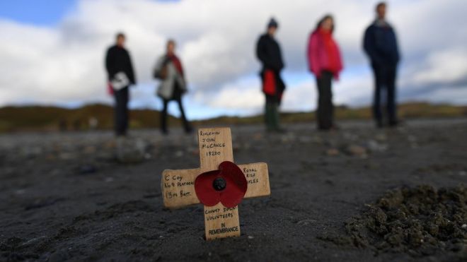 В песке посажен поминальный крест, когда добровольцы рисуют изображения убитых во время Первой мировой войны, части празднования Дэнни Бойла «Страницы моря», на пляже Мерло в Ньюкасле, Северная Ирландия.