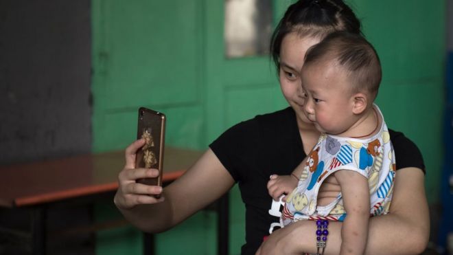 A woman takes a selfie with a baby on a street in Beijing