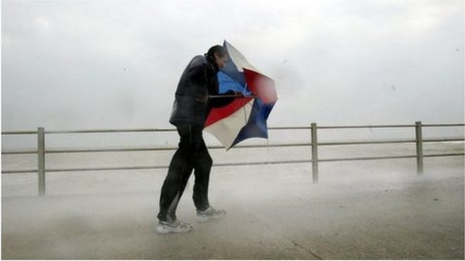 Мужчина держит зонтик в ветренную погоду