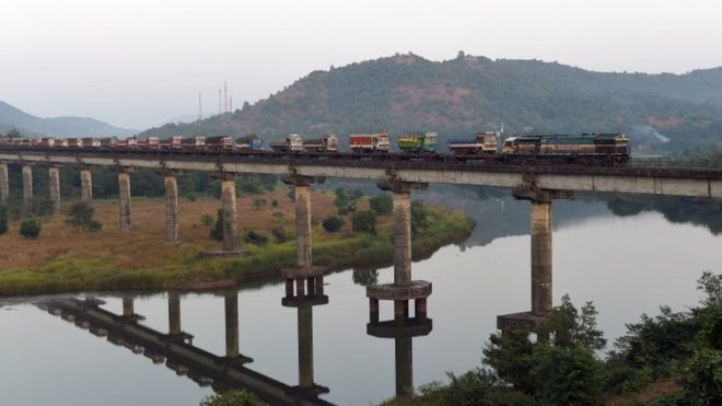 На этой фотографии, сделанной 30 ноября 2014 года, изображен дизельный локомотив индийских железных дорог, перевозящий железнодорожные вагоны с загруженными грузовиками на мосту Шаштри недалеко от Сангмешвара в Махарастре.