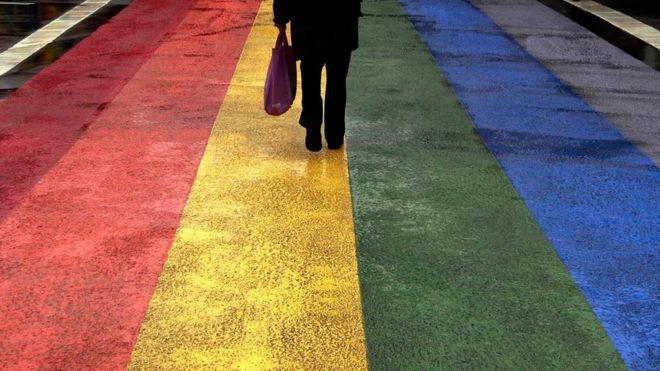 Pessoa anda sob rua pintada com cores do arco-íris.