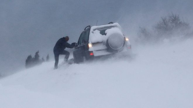 Мужчина пытается выкопать свою машину из снега