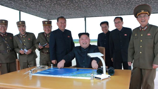 Ким Чен Ын, сидящий в центре за столом с картой, виден в окружении улыбающихся чиновников и военнослужащих на официальном фото