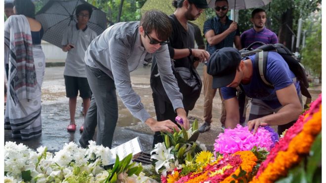 Люди дарят цветы, отдавая дань уважения жертвам нападения на пекарню Holey Artisan