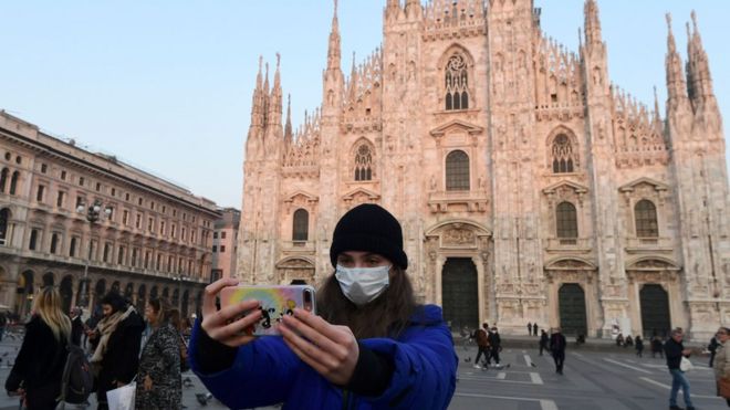 Турист в защитной маске делает селфи на площади Пьяцца дель Дуомо в Милане