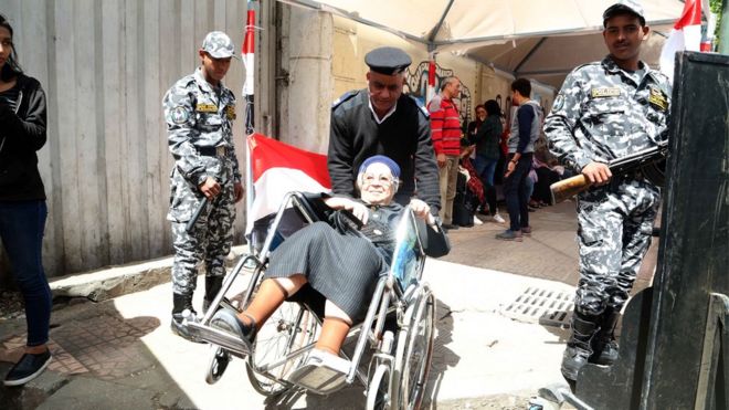 شرطي يدفع كرسي متحرك تجلس عليه امرأة مسنة