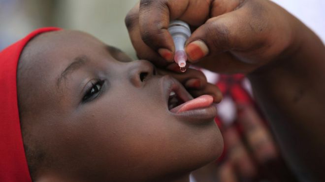 На этом снимке, сделанном в это воскресенье, 13 апреля 2014 года, неизвестный сотрудник здравоохранения вводит вакцину против полиомиелита ребенку в Каво-Кано, Нигерия.