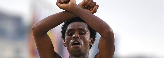 Фейса Лилеса из Эфиопии скрестила руки на голове на финише соревнований по марафону среди мужчин на Олимпийских играх 2016 года в Рио
