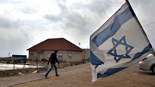 Hombre pasando frente a bandera de Israel en asentamiento.