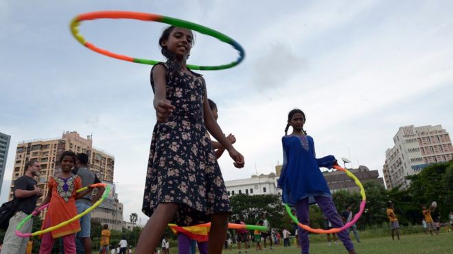Уличные дети играют в хула-хупы, в то время как другие играют в игру с членами британской команды по регби Harlequins F.C. в Калькутте 16 июня 2015 года.