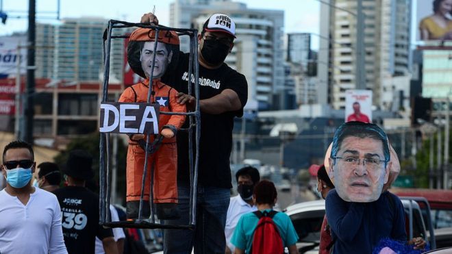 Militantes de la oposiciún muestran una figura con el rostro de Juan Orlando Hernández, tras unos barrotes, junto a un cartel de la DEA.