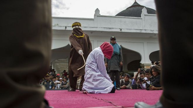 An Acehnese woman is lashed by a hooded local government officer during a public caning at a square in Aceh province, on June 12, 2015.