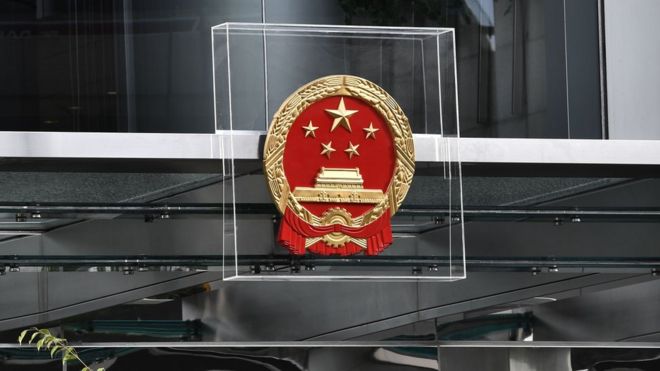 Офицеры полиции охраняют эмблему китайского офиса связи, защищенную плексигласом во время демонстрации в Гонконге 28 июля 2019 года.