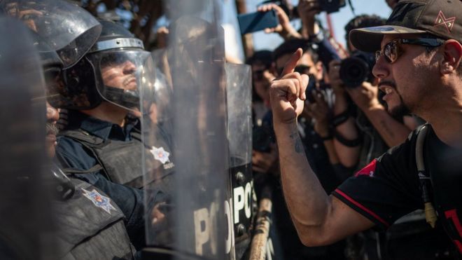 Демонстрант, участвующий в марше протеста против мигрантов, кричит на полицейскую линию в мятежном снаряжении, которая охраняла временное убежище, в котором находился караван из Центральной Америки, пытающийся добраться до США, в Тихуане, Мексика