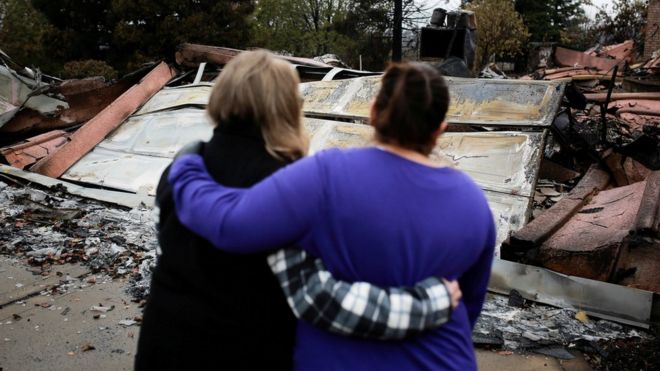 Жители утешают друг друга, глядя на останки своих домов в Раю 22 ноября 2018 года